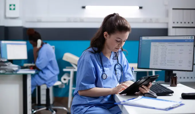 Nurse working with technology at hospital desk with stethoscope around their neck