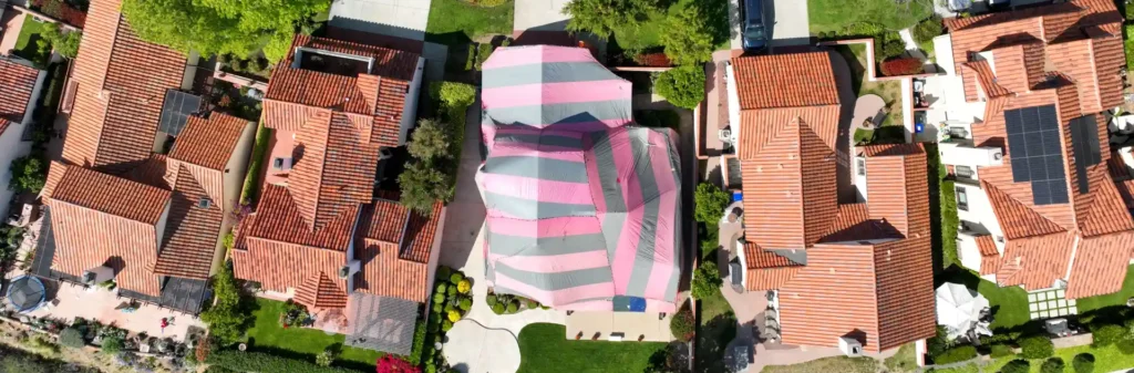 Aerial view of residential neighborhood with middle house wrapped in fumigation tarp