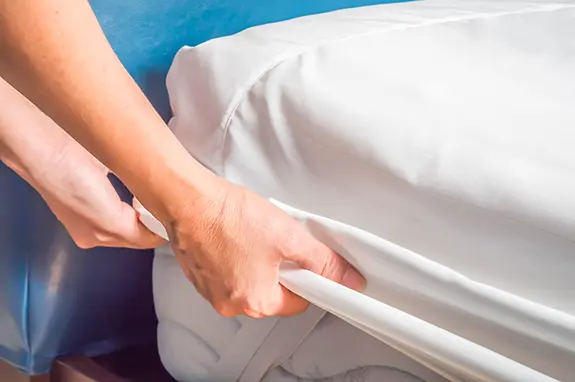 Person pulling a cover onto a bed mattress