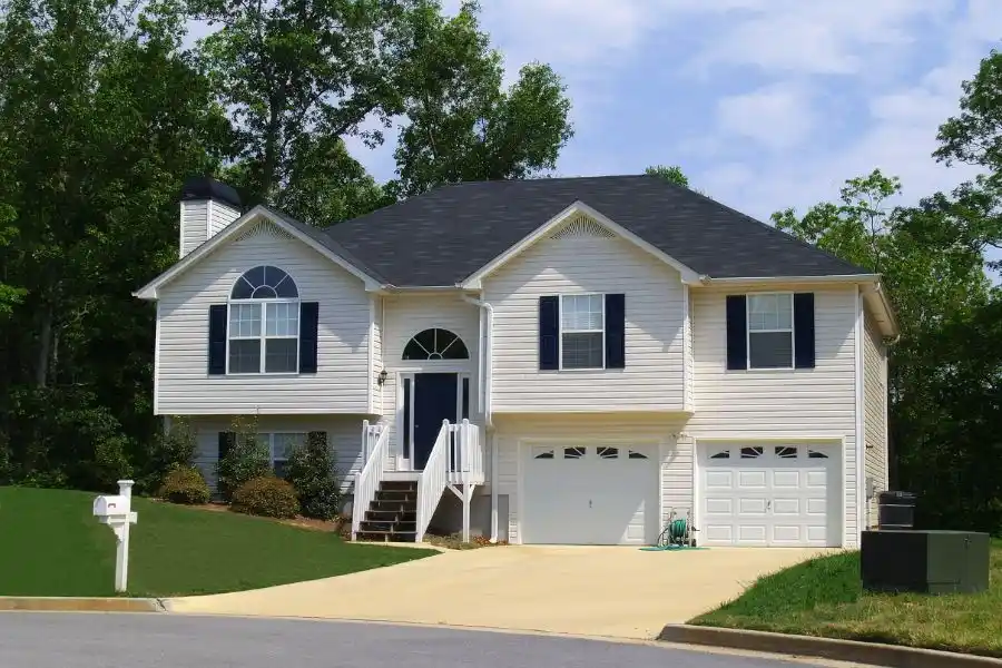 Exterior view of a suburban split-level house with white siding and a green lawn, representing a property under inspection.