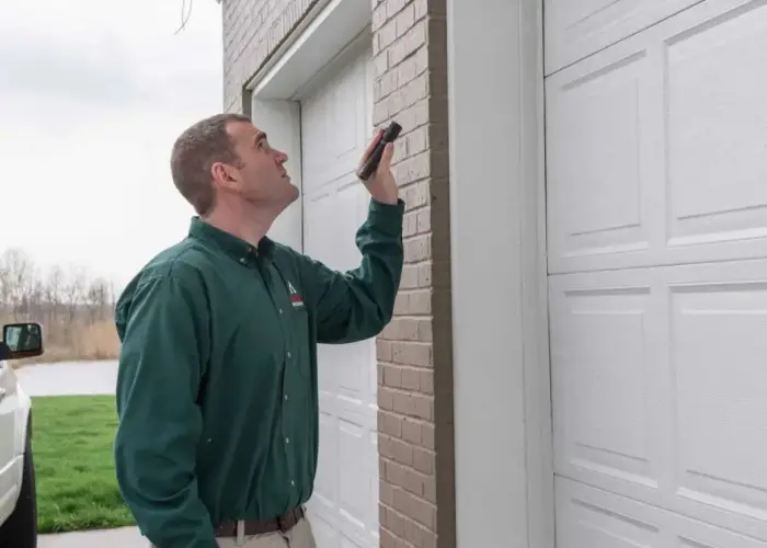 An Action Pest Control, Inc. technician shines a flashlight under a new garage exterior in search of signs of termites