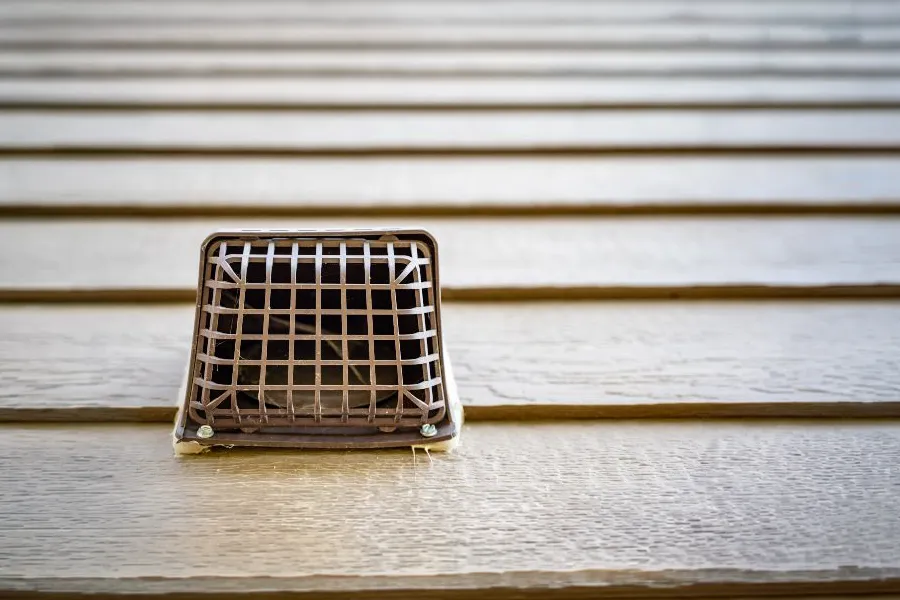 A protective wire mesh vent cover installed on house siding to keep mice away and prevent pest entry.