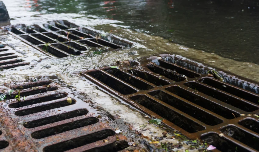 Low-angle close-up of heavy runoff water rushing through the rusty iron drainage grates of a commercial business.